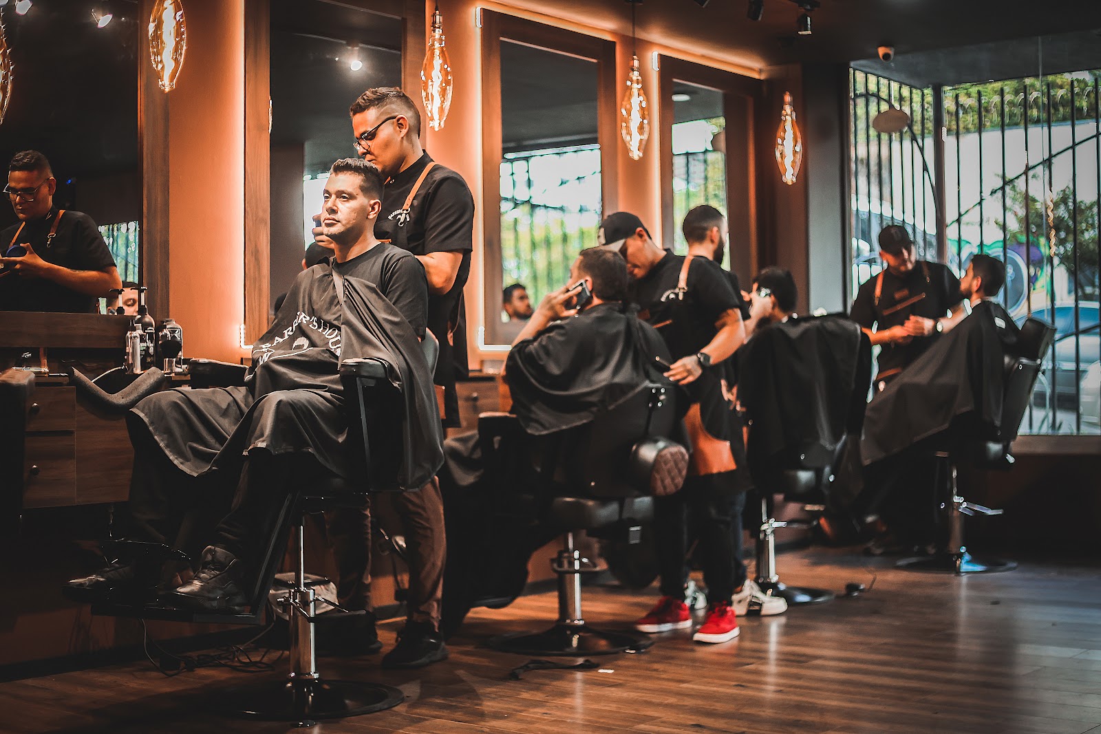 Cuatro barberos de Barber's House atendiendo a la vez, bajo los bombillos colgantes