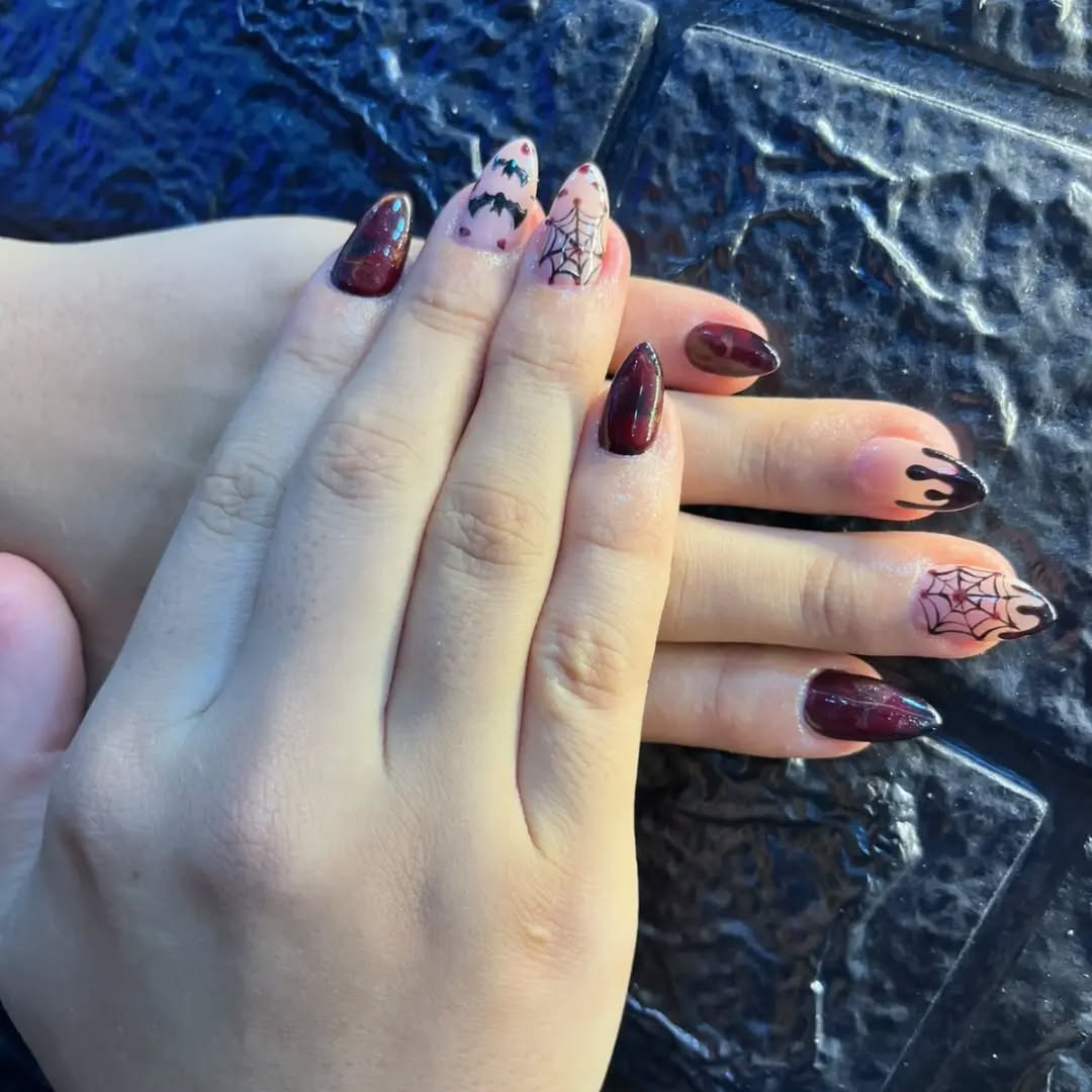 Manos con uñas stiletto vino tinto, telarañas y murciélagos sobre pared negra