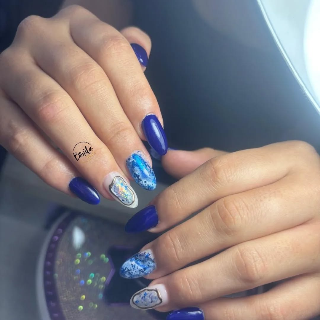 Dos manos con uñas azul rey y diseños de efecto piedra y foil