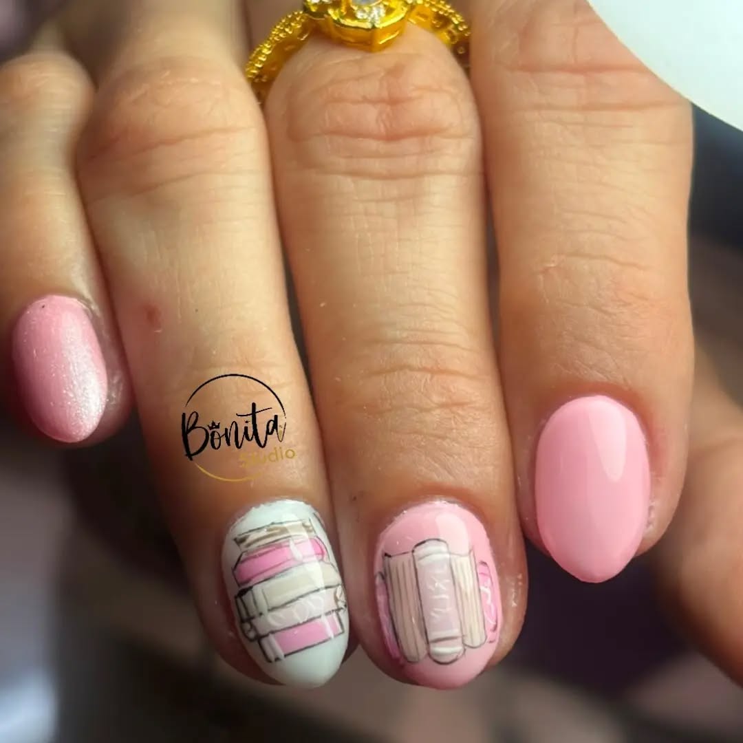 Uñas cortas rosadas con libros ilustrados en dos uñas y anillo dorado