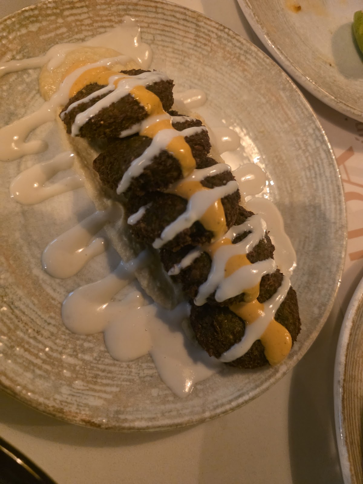 Falafel en fila sobre plato texturizado, con salsa blanca y salsa amarilla