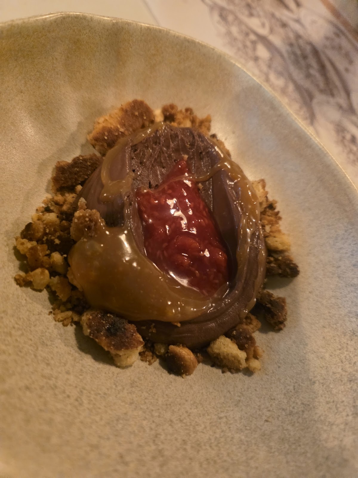 Postre de chocolate con mermelada de frambuesa, caramelo y crocante en plato beige