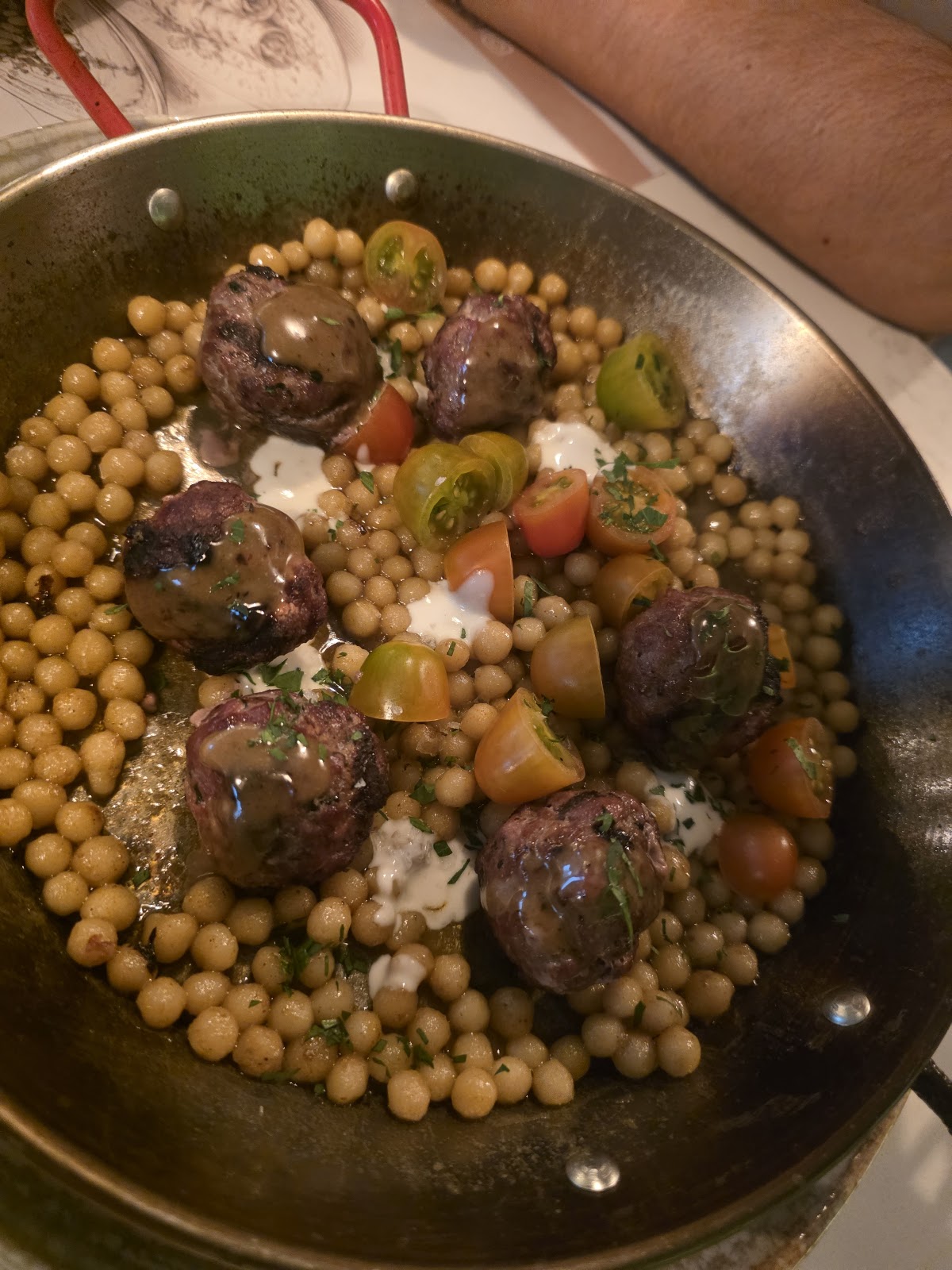 Albóndigas con cuscús perla y tomates cherry en sartén metálica de asa roja