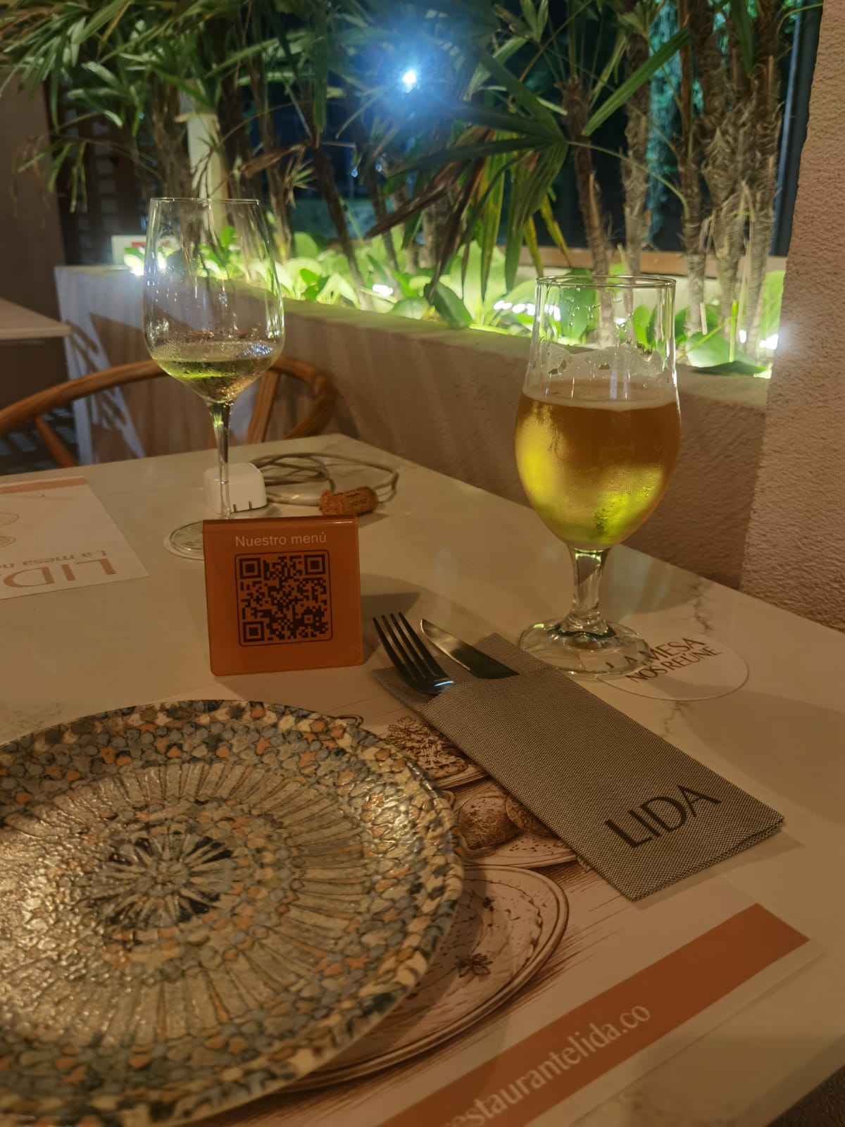 De noche: vino blanco, cerveza, menú QR y servilleta LIDA sobre la mesa